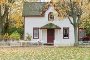 A small whitehouse with a white fence and a few trees